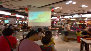 家长陪伴孩子在潍坊银座美食广场观看动画片 家长陪伴孩子在潍坊银座美食广场观看动画片